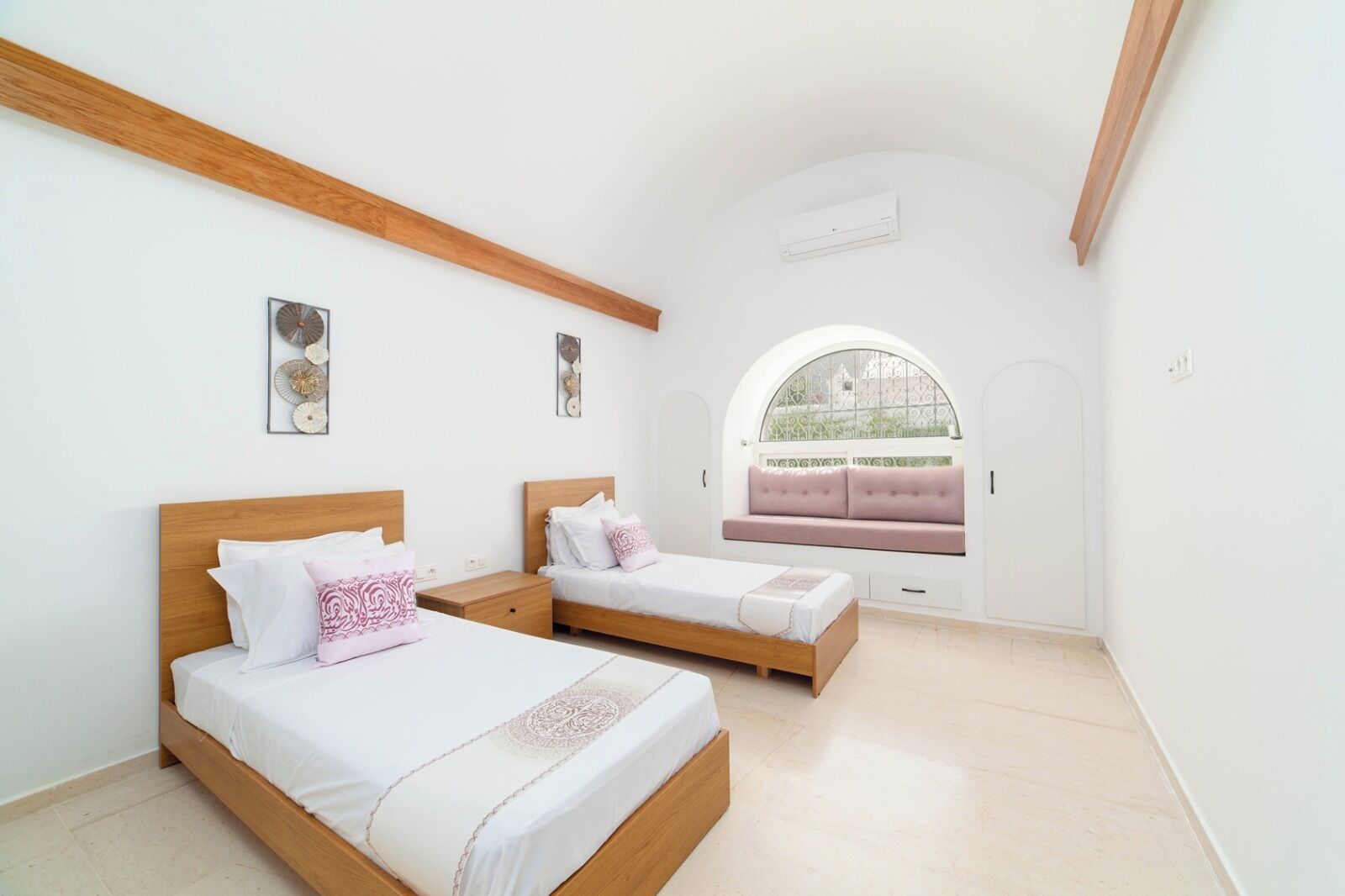A bedroom with two beds, a window seat, and a ceiling fan.