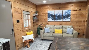A cozy cabin interior with a wooden interior, a sofa, a dining table, and a kitchen area. - Cozy Cabin - Fire pit, Upscale Area, Near I44 & HWY 65 (Springfield)