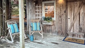 A rustic wooden porch with two rocking chairs, a ladder, a window with a view, and a door with a doormat. - Cozy Cabin - Fire pit, Upscale Area, Near I44 & HWY 65 (Springfield)