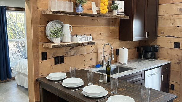 A modern kitchen with wooden cabinetry, a central island with bar seating, and a variety of kitchen appliances. - Cozy Cabin - Fire pit, Upscale Area, Near I44 & HWY 65 (Springfield)