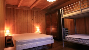 A wooden cabin room with two bunk beds, a wooden ceiling, and two bedside lamps.