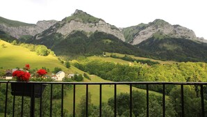A balcony with a view of a mountainous landscape, including green fields and a house.
