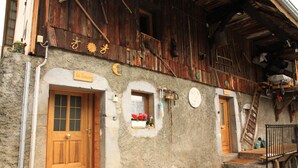 A rustic building with a wooden door, a small window with flowers, and a staircase leading to a loft area.