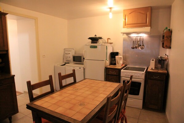 A compact kitchen with a dining table, chairs, a refrigerator, a microwave, a coffee maker, a stove, and a sink.