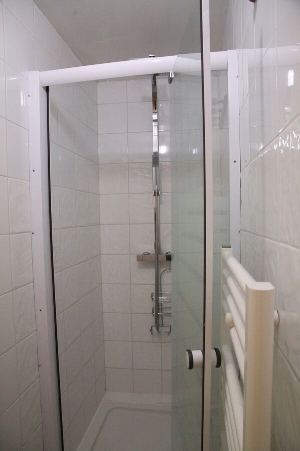 Un box de ducha con paredes de azulejos blancos y un perchero blanco.