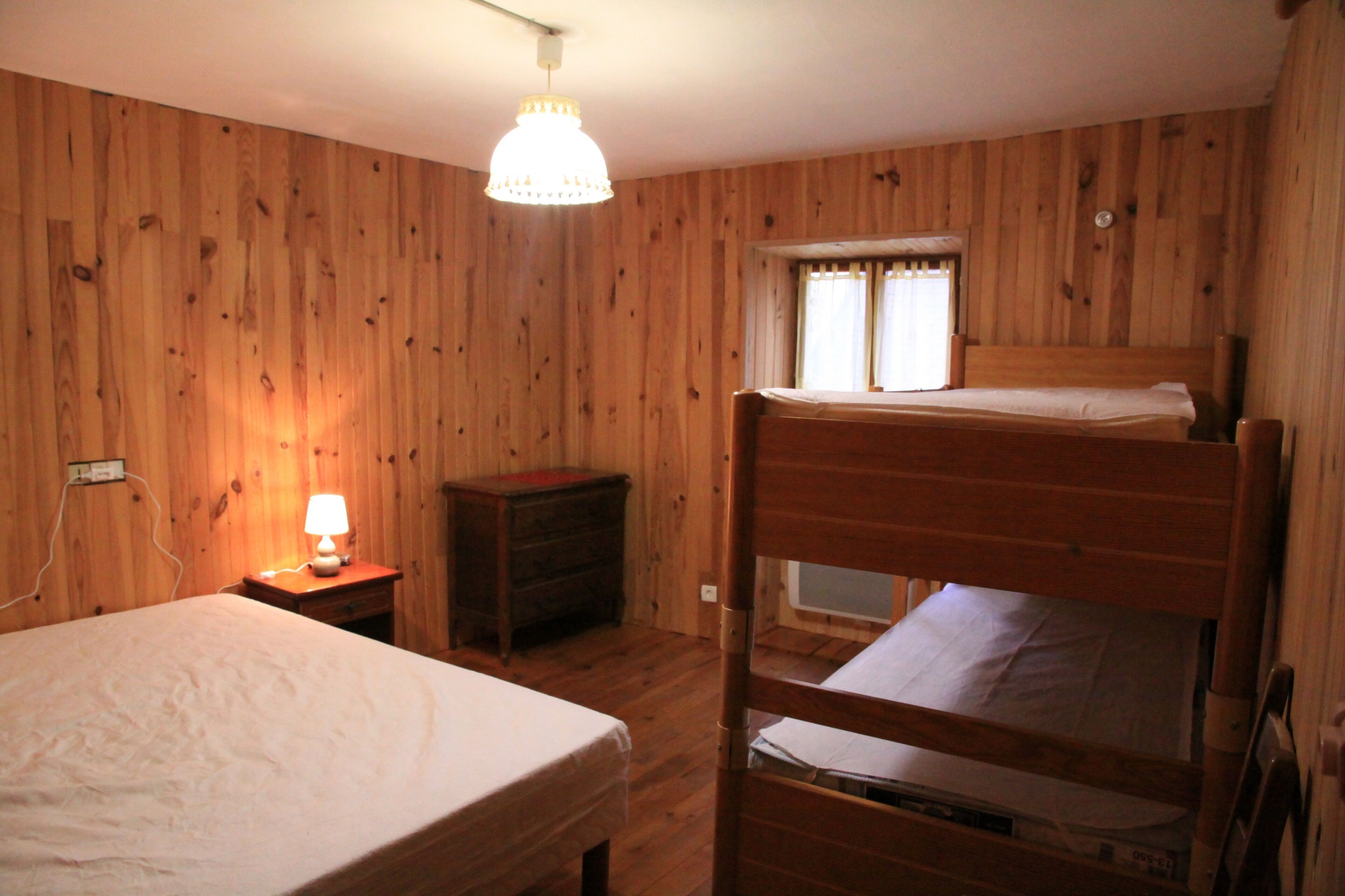 Ein Zimmer mit Holzwänden, einem Etagenbett, einem Nachttisch mit Lampe und einem Vorhangfenster.