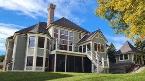 Une grande maison à deux étages, dotée d’une cheminée imposante, d’un porche couvert et d’un escalier menant à l’étage supérieur.