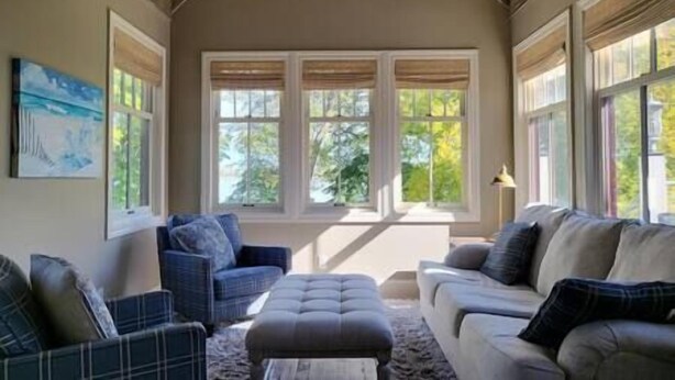 Un salon avec un plafond haut, de grandes fenêtres, un canapé, un fauteuil et un tapis.