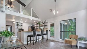 A spacious kitchen with a high ceiling, modern lighting, and a large window offering a view of greenery. - Cozy Whispering Hideaway- Indulge in serenity and unwind in nature. (Ponchatoula)