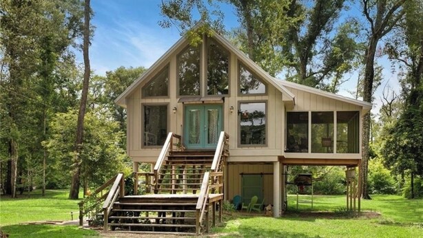 A two-story wooden cabin with a front porch, a staircase, and a covered area with a table and chairs. - Cozy Whispering Hideaway- Indulge in serenity and unwind in nature. (Ponchatoula)