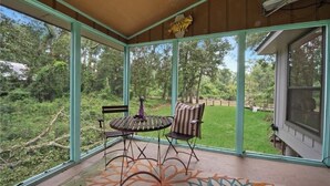 A covered patio with a table and chairs, a decorative bird sculpture, and a view of a grassy yard. - Cozy Whispering Hideaway- Indulge in serenity and unwind in nature. (Ponchatoula)