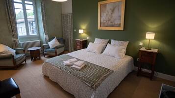 Habitación de hotel con una cama grande, dos mesitas de noche con lámparas, una silla, una pequeña mesa y un radiador.