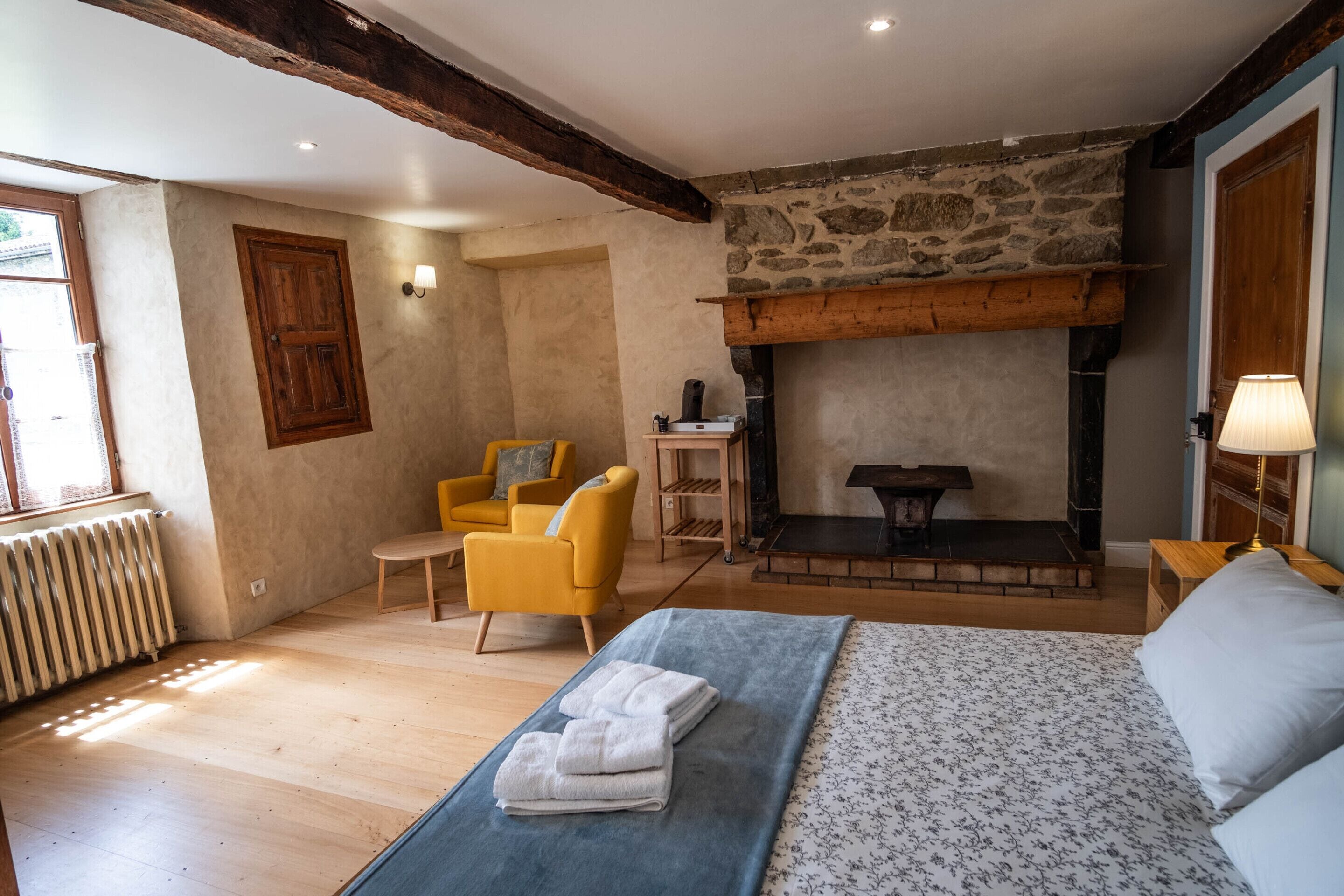 Un dormitorio con cama, chimenea, un sillón amarillo, un banco de madera y un radiador.