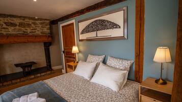 Une chambre à coucher avec un lit, des oreillers, une table de chevet, une lampe, une cheminée et un tableau encadré au mur.