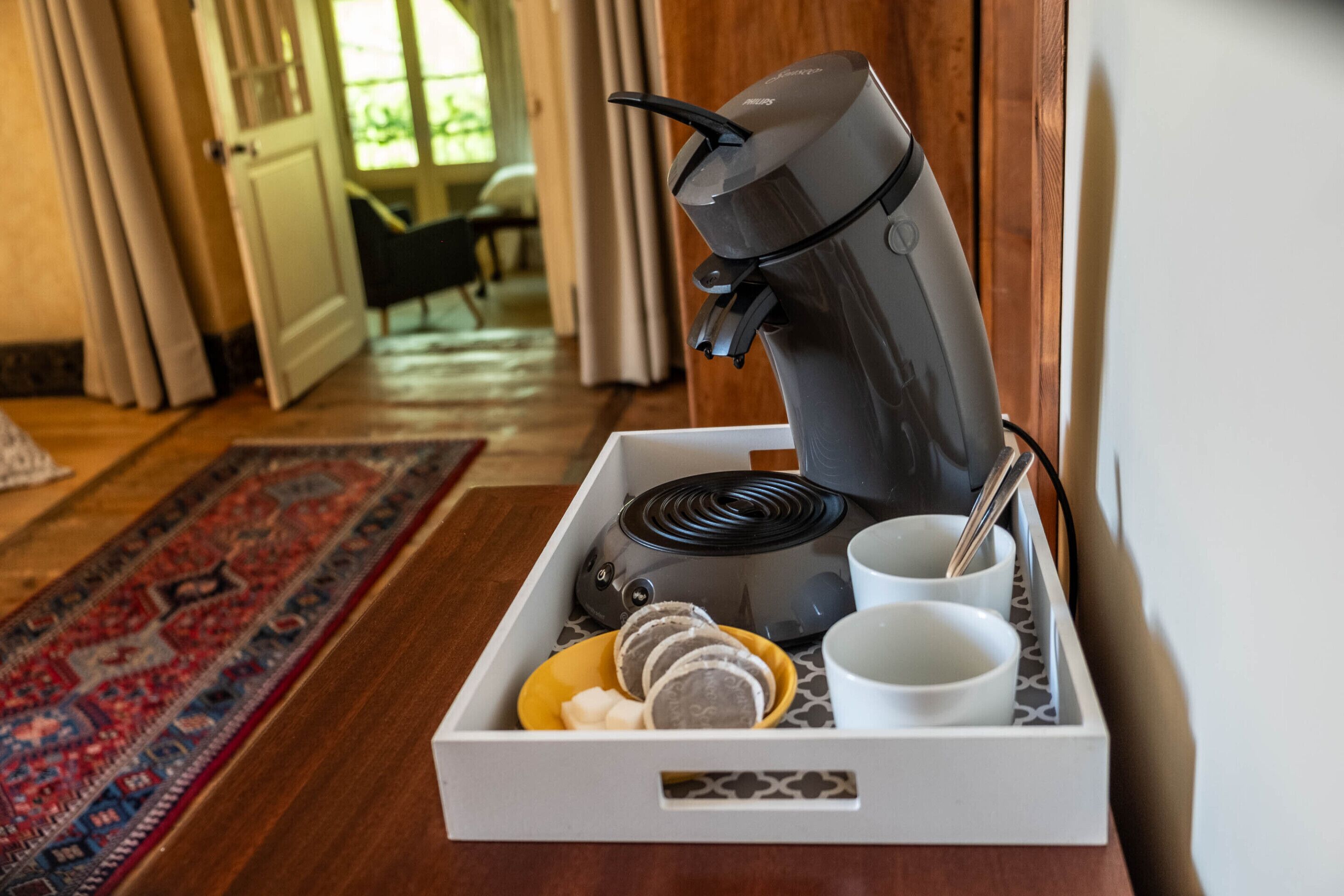 A coffee maker with a tray containing cups, a spoon, and a plate with food items.