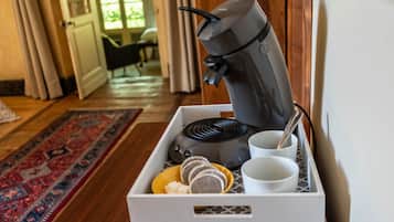 A coffee maker with a tray containing cups, a spoon, and a plate with food items.
