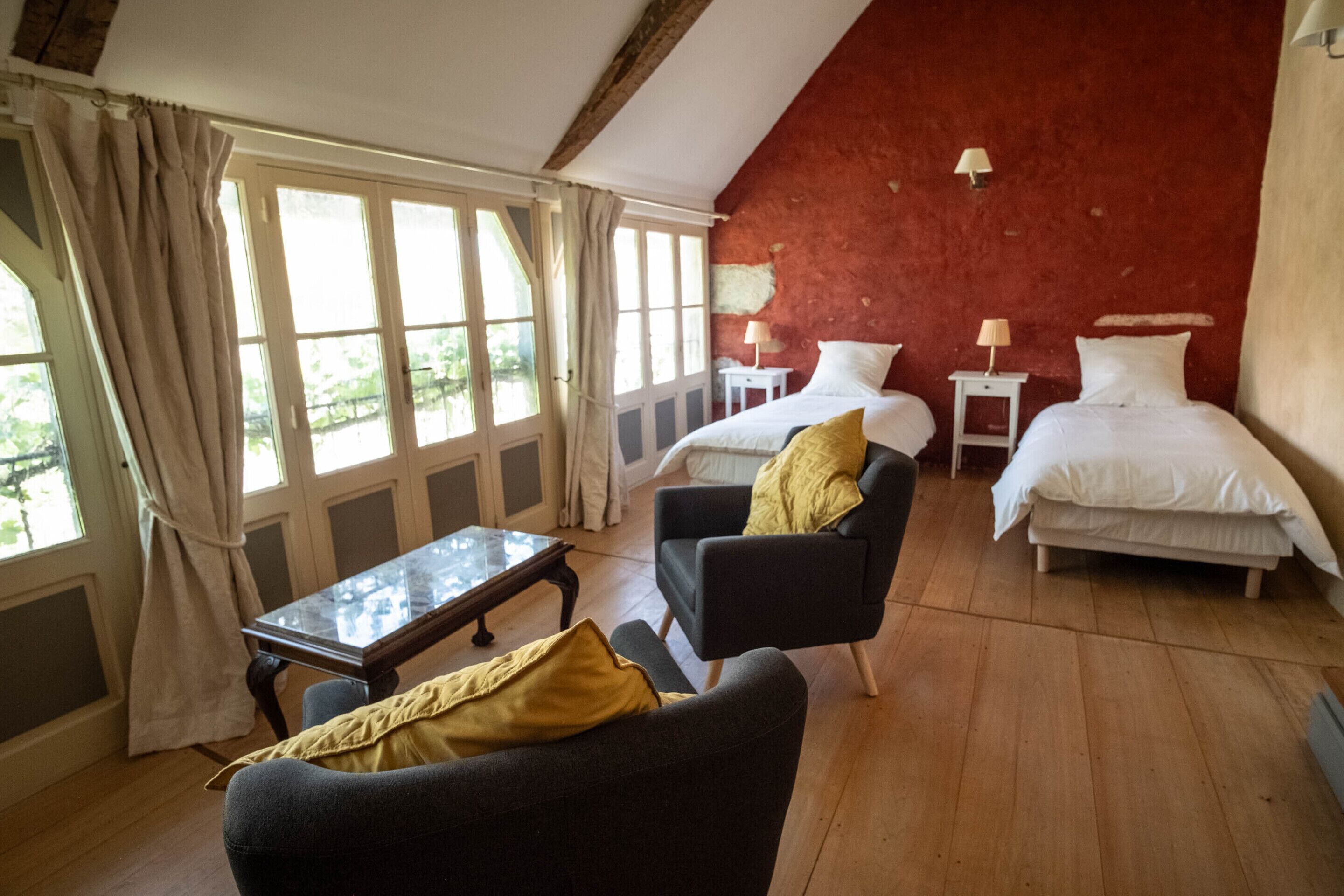 Un dormitorio con dos camas, un sofá, una mesita y una ventana con cortinas.