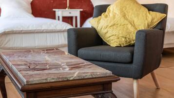 A room with a bed, a grey armchair with a yellow pillow, and a wooden coffee table with a marble top.