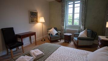 Een hotelkamer met een bed, twee fauteuils, een klein tafeltje, een lamp, een schilderij aan de muur en een raam met gordijnen.