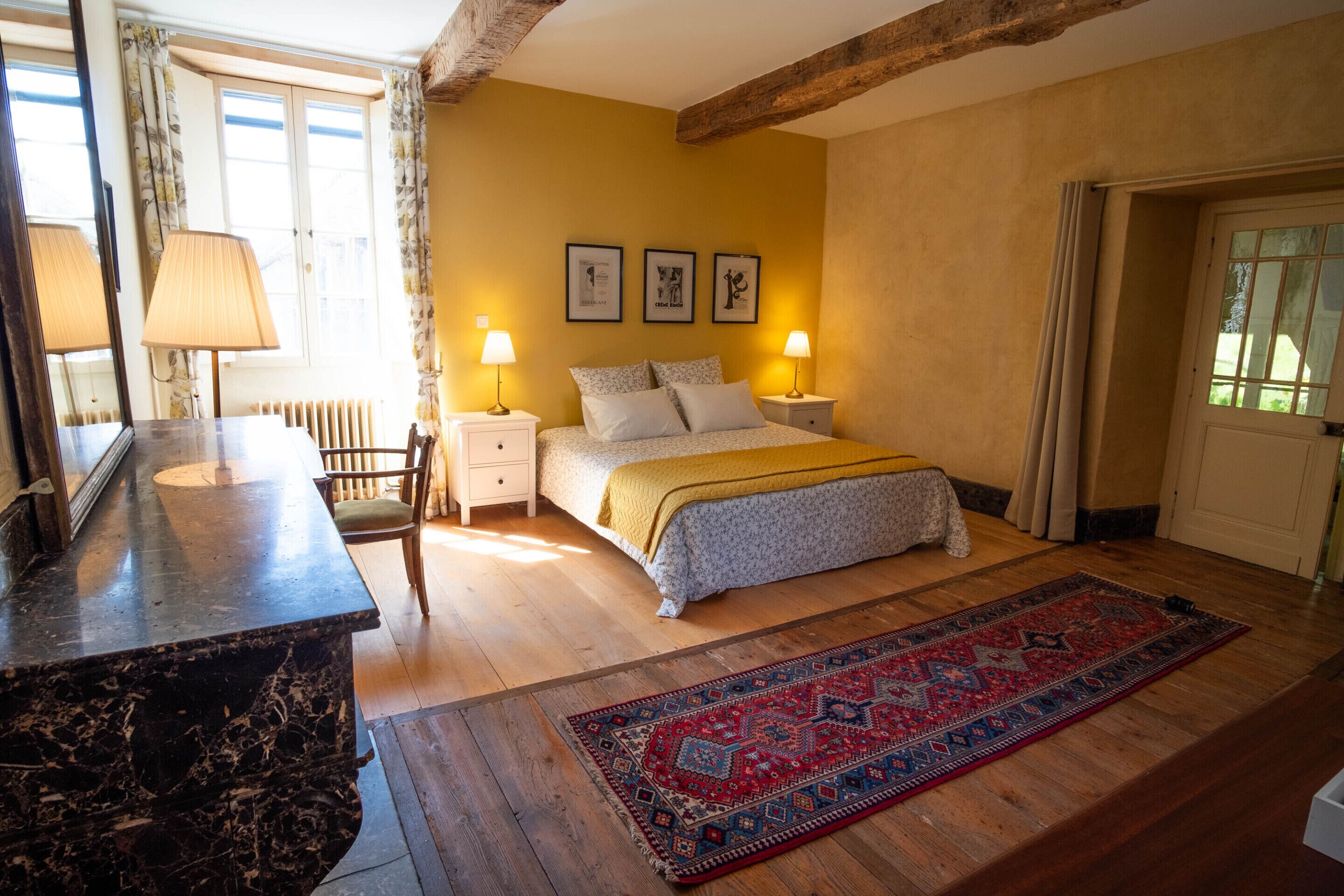 A bedroom with a bed, bedside lamps, a nightstand, a dresser, a mirror, a window with curtains, and a rug.