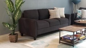 A living room with a dark sofa, a coffee table, a potted plant, and a painting on the wall.