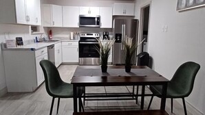 A modern kitchen with white cabinets, stainless steel appliances, and a dining area with a wooden table and green chairs.