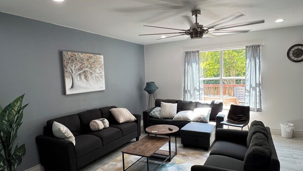 A modern living room with a ceiling fan, two sofas, a coffee table, and a large window with curtains.