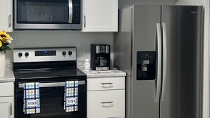 A modern kitchen with white cabinets, a stainless steel refrigerator, a microwave, an oven, and a coffee maker.