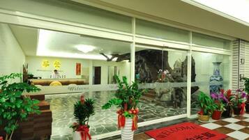 Zona de recepción de hotel con mostrador de check-in, escritorio de recepción y plantas en macetas.