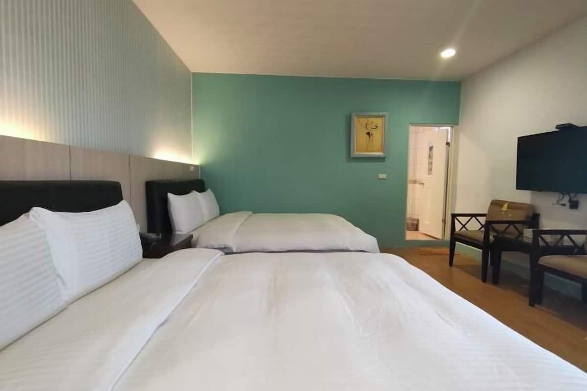 A hotel room with two beds, a desk, a chair, a television, and a door.