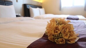 A hotel room with a neatly made bed, a bouquet of flowers, and a window with daylight.