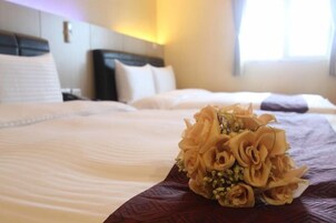 Una habitación de hotel con una cama bien hecha, un ramo de flores y una ventana con luz diurna.