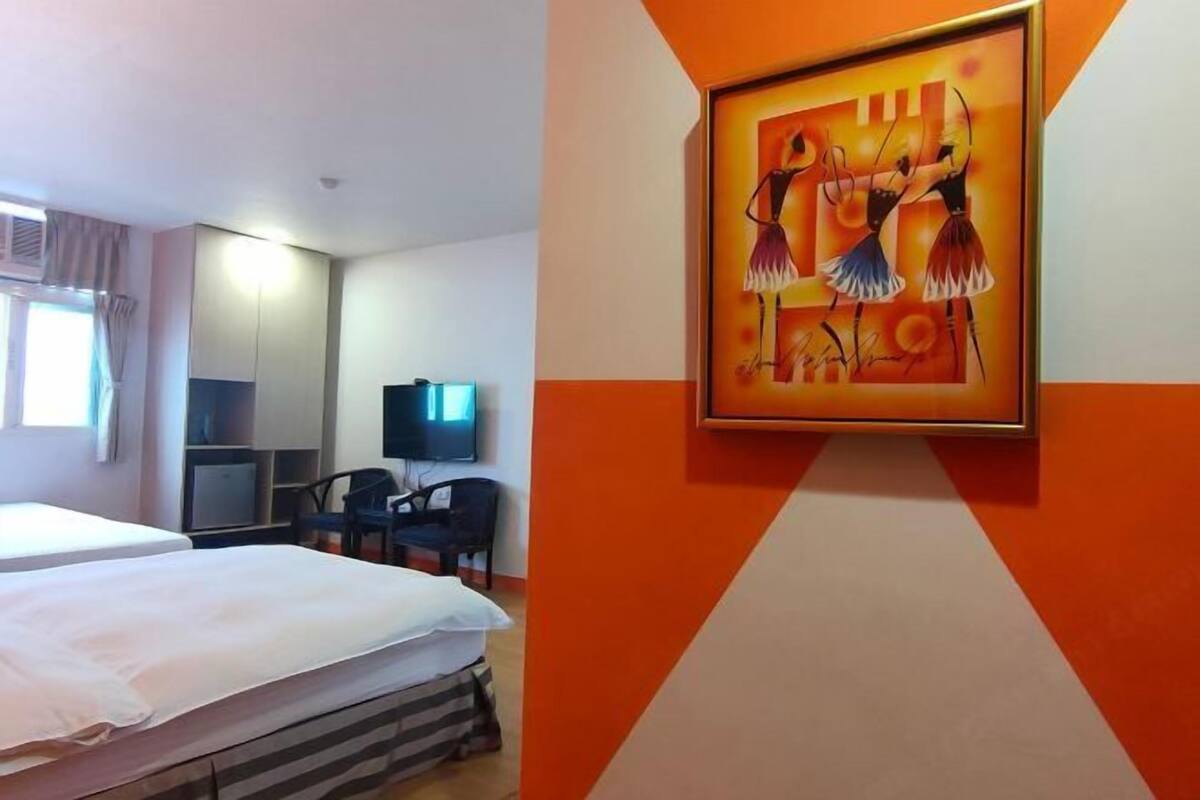 A hotel room with a bed, a desk, a chair, a television, and a painting on the wall.