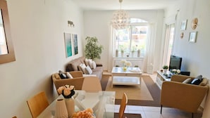 Un salon moderne avec une table à manger en verre, deux canapés, une table basse et un téléviseur.