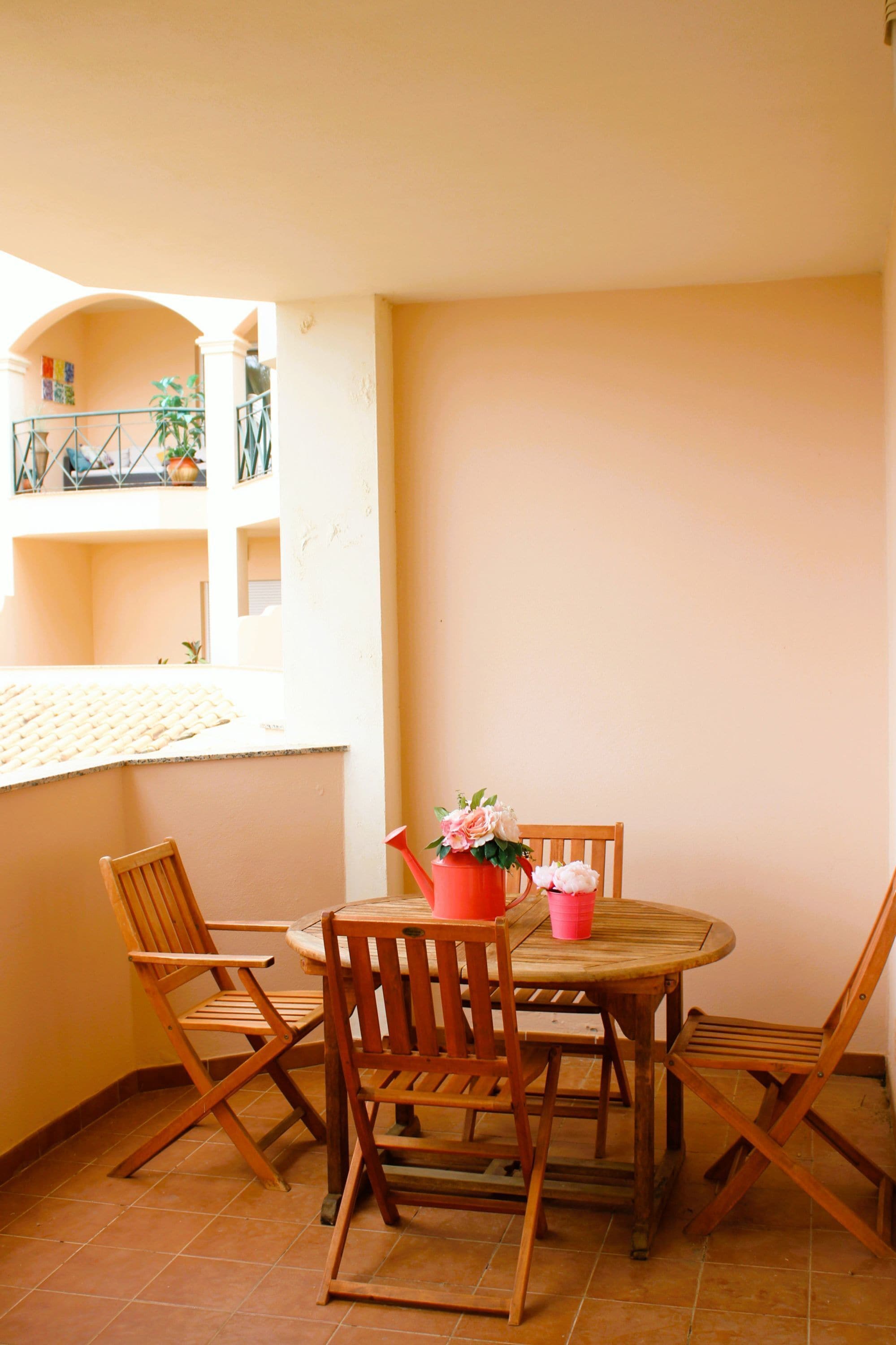 Una mesa de madera redonda con cuatro sillas, una planta en maceta y una taza rosa sobre la mesa.