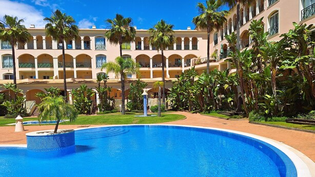 Un hôtel doté d’une grande piscine entourée de palmiers et d’un jardin bien entretenu.