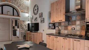 A modern kitchen with wooden cabinets, a stone wall, and a large clock on the wall. - Katrin House Alla Marina di Cefal by Wonderful Italy (Cefalù)