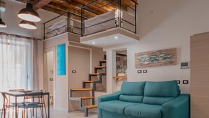 A spacious living area with a teal sofa, wooden staircase, and a dining table with chairs. - Katrin House Alla Marina di Cefal by Wonderful Italy (Cefalù)