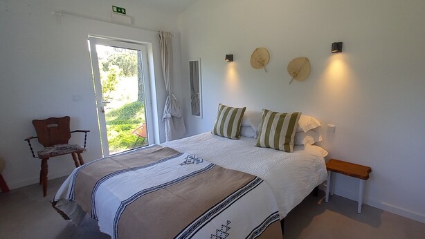 A bedroom with a bed, a chair, a bedside table, and a window with curtains. - Monte da Urze (Aljezur)