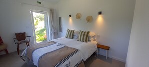 Ein Schlafzimmer mit Bett, Stuhl, Nachttisch und einem Fenster mit Vorhängen.