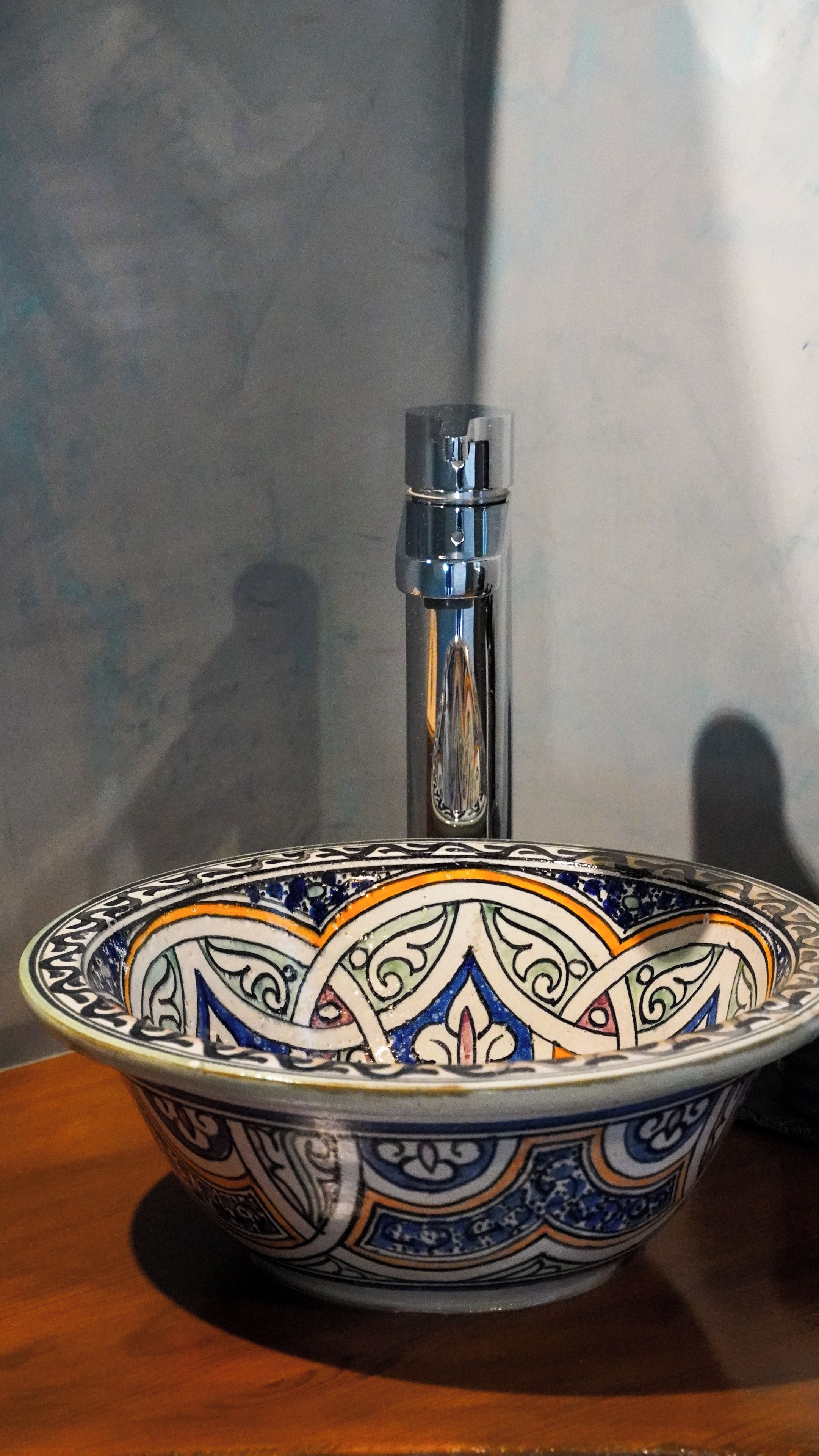 A ceramic bowl with intricate patterns and a metallic faucet.