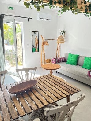 A room with a wooden table and chairs, a sofa with green cushions, and a hanging plant. - Monte da Urze (Aljezur)