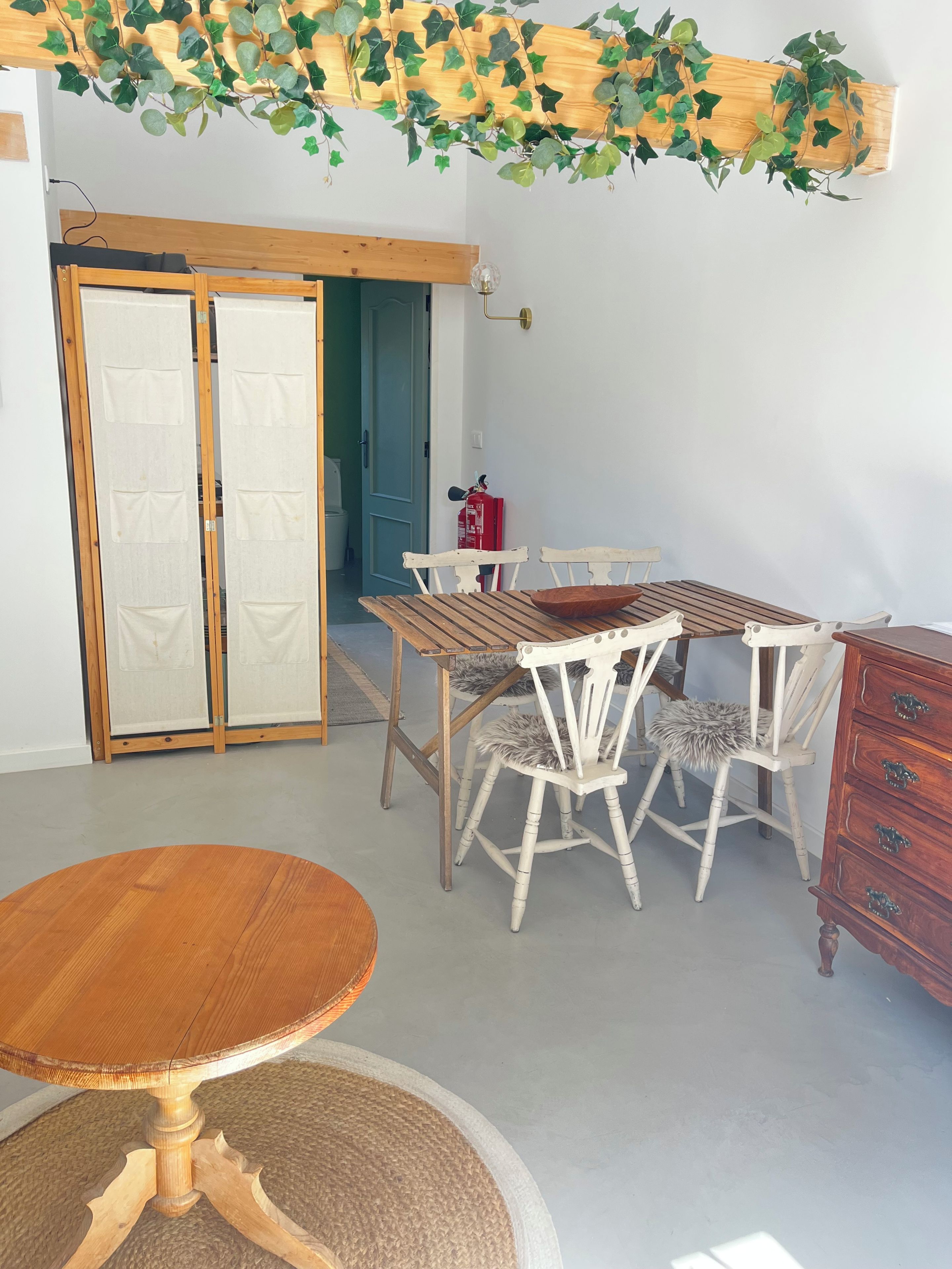 A room with a wooden dining table, white chairs, a wooden cabinet, and a door with a frosted glass panel.
