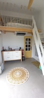 Una habitación compacta con una cama litera, una kitchenette con pileta y estufa, un tapete redondo tejido, y una puerta con ventanal.