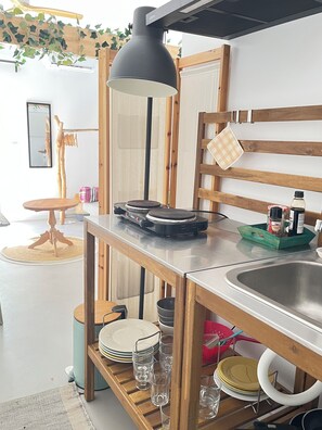 Una cocina con una mesa de madera, una lámpara colgante negra, un lavamanos y diversos utensilios de cocina.