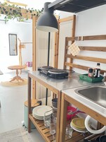 Una cocina con una mesa de madera, una lámpara colgante negra, un lavamanos y diversos utensilios de cocina.