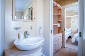 Ein Badezimmer mit Waschbecken, Spiegel und Handtuchhalter. Ein Holzschrank und eine Tür zu einem Schlafzimmer mit Bett und Nachttisch sind ebenfalls vorhanden.