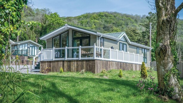 Ein eingeschossiges Haus mit Terrasse, umgeben von üppiger Vegetation und einer Erhebung im Hintergrund.