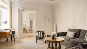 Una sala de estar con un sofá, una mesa redonda de centro, un escritorio y una silla. Hay una puerta que conduce a otra habitación.