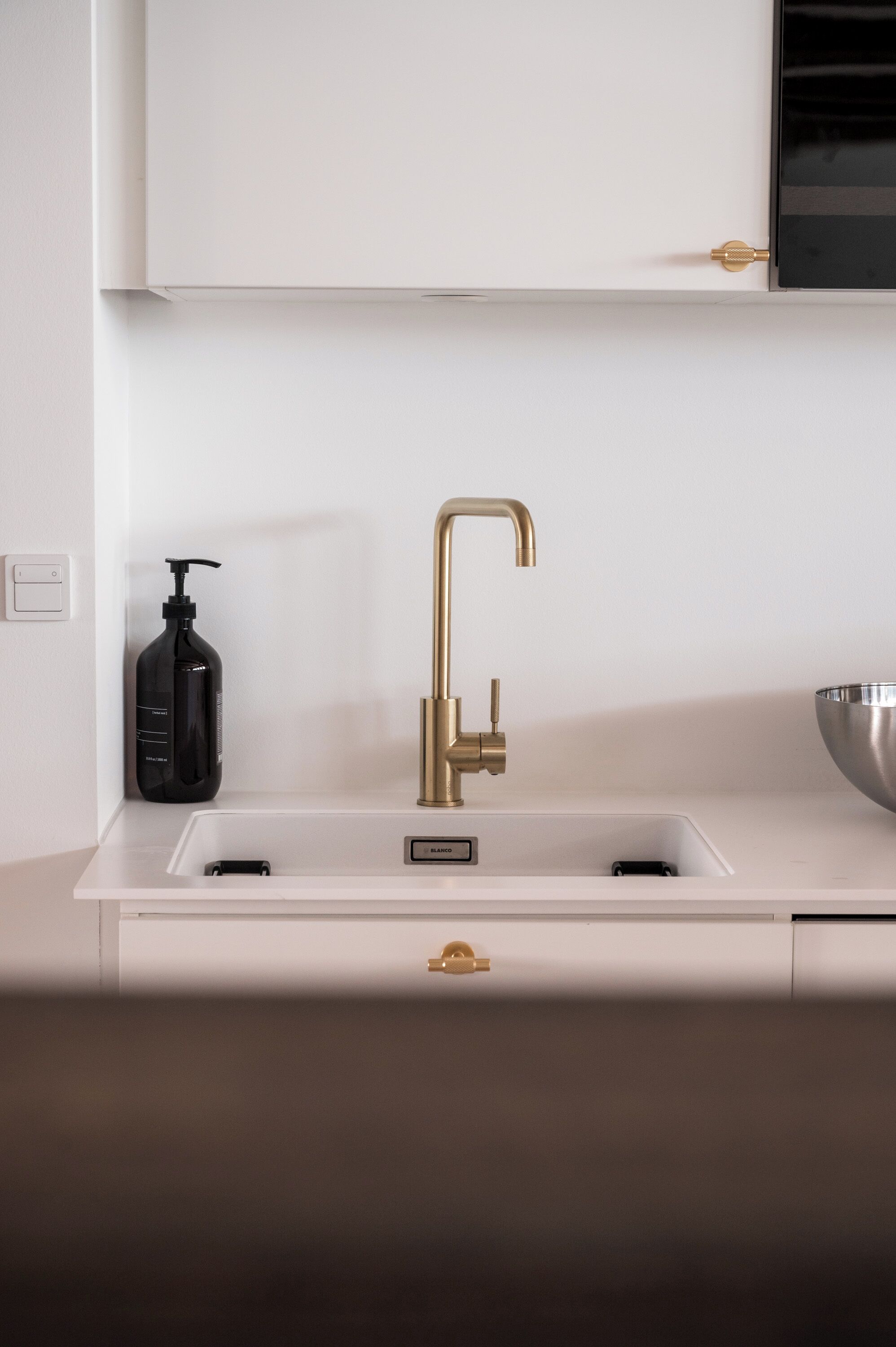 A modern kitchen with a white countertop, a gold faucet, and a black soap dispenser.